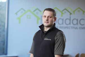 A male Broadacres colleague in a Broadacres uniform stands in front of a Broadacres logo.